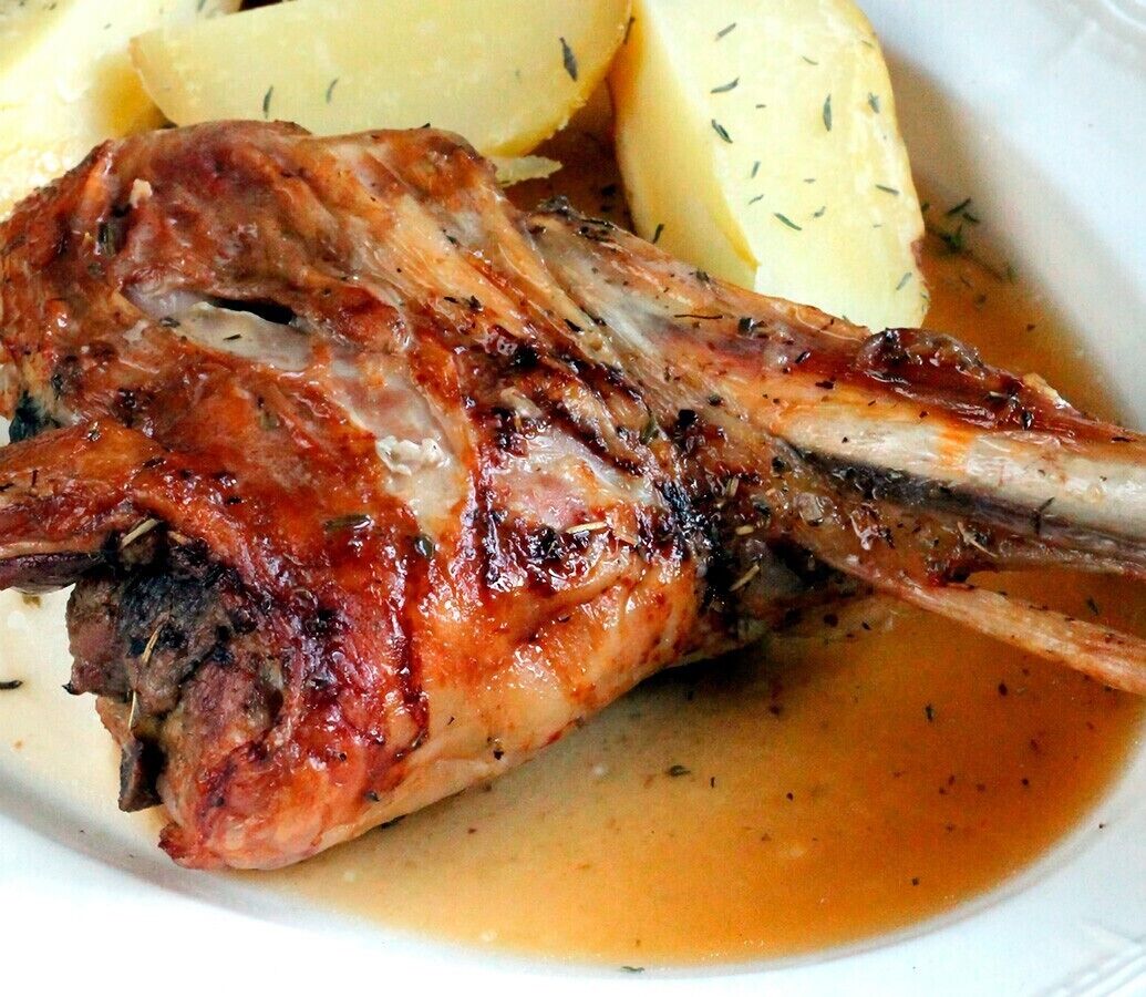 A roasted lamb leg with a sauce, accompanied by boiled potatoes.