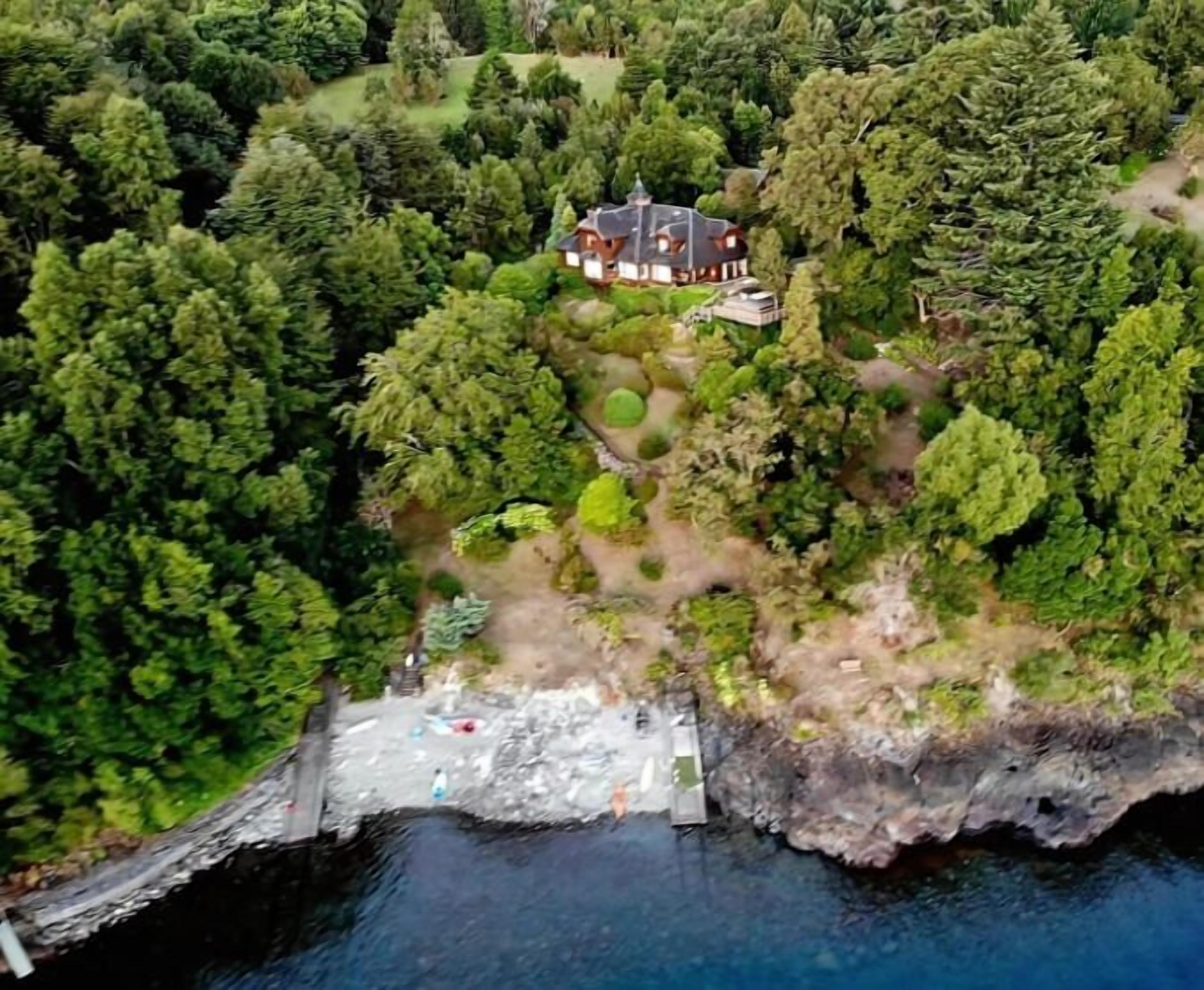Eine Luftaufnahme eines Hauses, das von dichtem Wald umgeben ist, mit einem Steg, der sich ins Wasser erstreckt.
