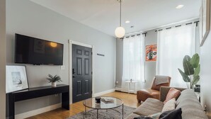 Una sala moderna con un televisor de pantalla plana, una puerta oscura, una mesa de centro redonda, un sofá y una planta grande.