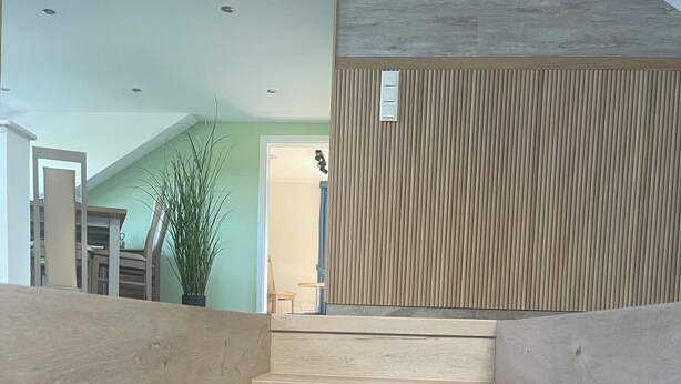 A wooden staircase with a modern design, leading to a room with a green wall and a wooden panel wall.