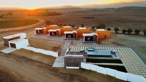 Un complexe hôtelier moderne doté de plusieurs chalets aux toits orange, d’une piscine et d’un chemin de terre qui traverse le domaine.