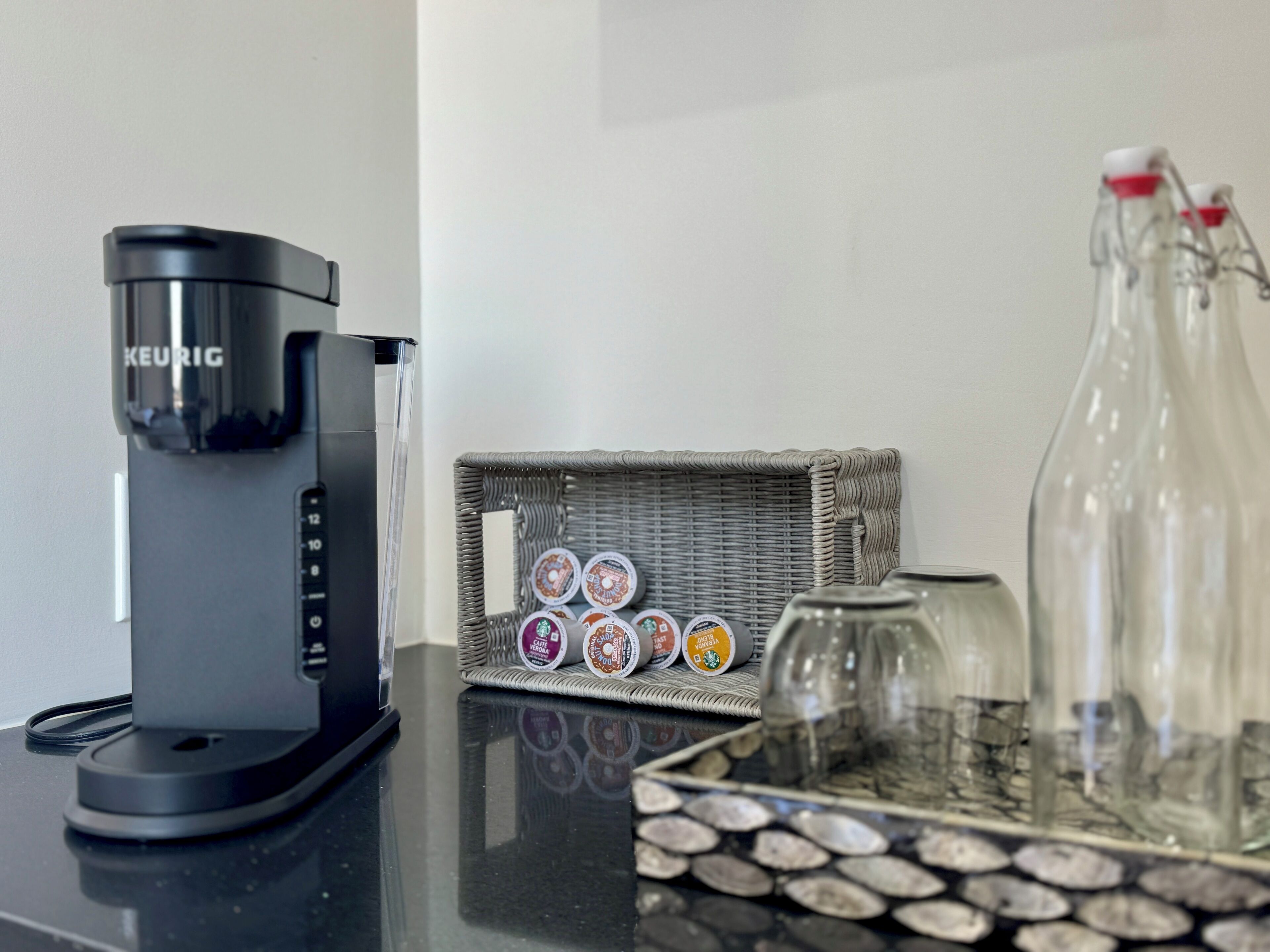 Una cafetera Keurig, un cesto con cápsulas de café y una botella de vidrio sobre una encimera.