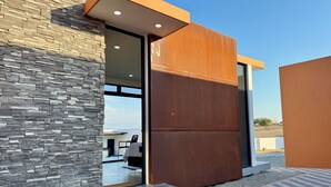 Un bâtiment moderne doté d’une façade en pierre, de grandes portes vitrées et d’un panneau métallique.