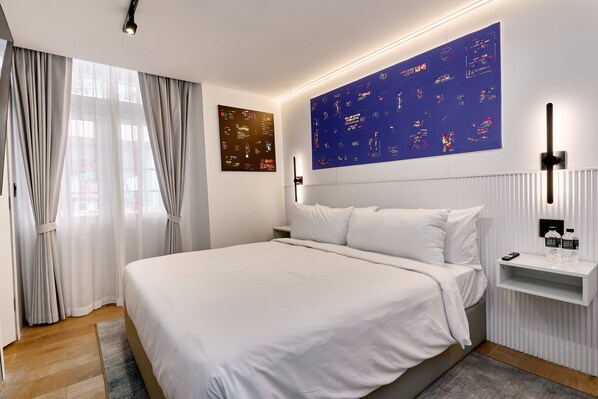 Una habitación de hotel moderna con una cama grande, un televisor montado en la pared y una mesita de noche con una botella y un control remoto.
