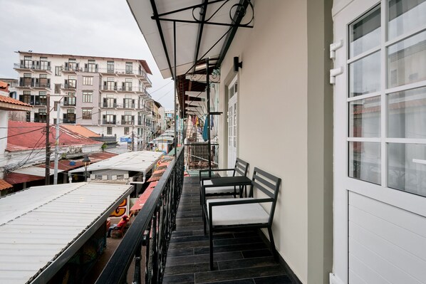 Un balcon offrant une vue sur le paysage urbain, avec des bâtiments dotés de balcons et d’un toit recouvert de tuiles.