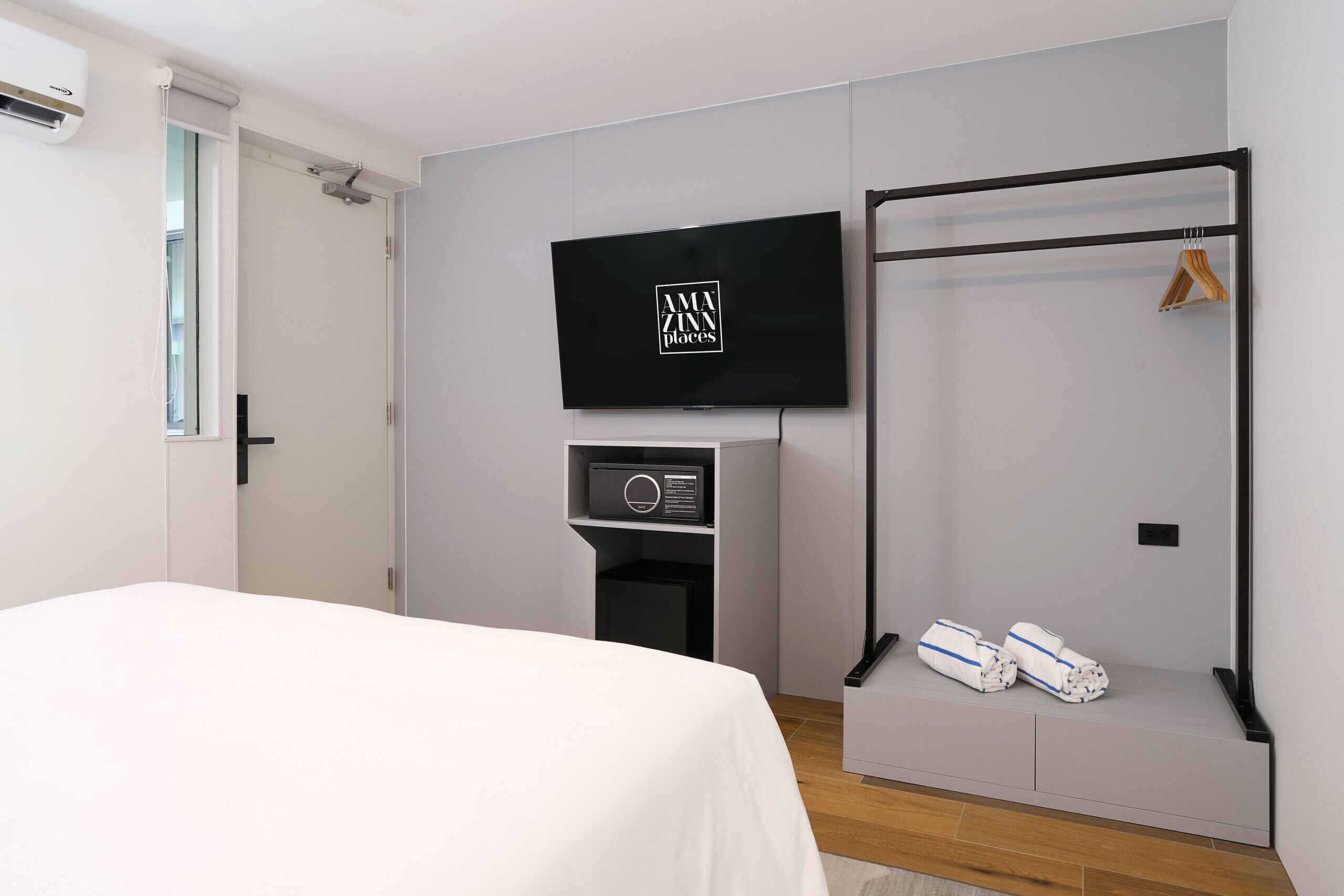 A hotel room with a bed, a TV mounted on the wall, a built-in safe, and a towel rack with towels.