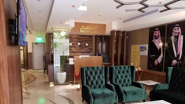 A lobby with a reception desk, green upholstered seating, a marble floor, and a large mirror with a portrait.