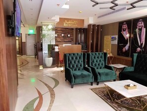 A lobby with a reception desk, green upholstered seating, a marble floor, and a large mirror with a portrait. - Palette Al Louloah Al Baraqah Aparthotel (Jeddah)
