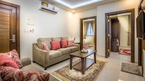 A living room with a sofa, coffee table, and a mirror. There is an air conditioning unit on the wall and a door leading to another room.