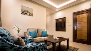 A living room with a sofa, a coffee table, a TV mounted on the wall, and a wooden door.