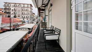 Un balcon offrant une vue sur le paysage urbain, avec des bâtiments dotés de balcons et d’un toit recouvert de tuiles.
