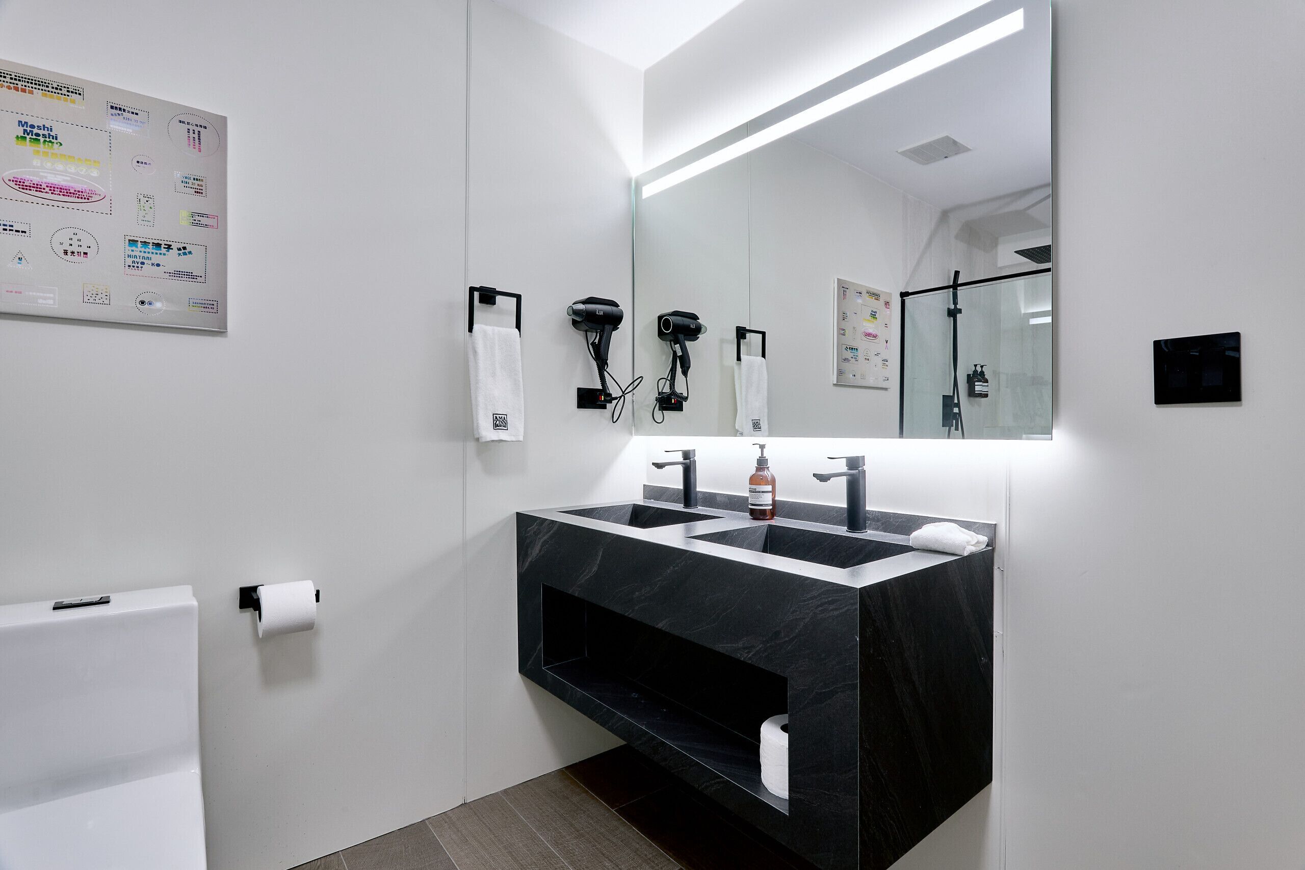 Un baño moderno con un lavamanos de mármol negro, dos secadores de pelo y un espejo grande.