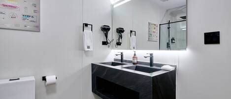 Un baño moderno con un lavamanos de mármol negro, dos secadores de pelo y un espejo grande.
