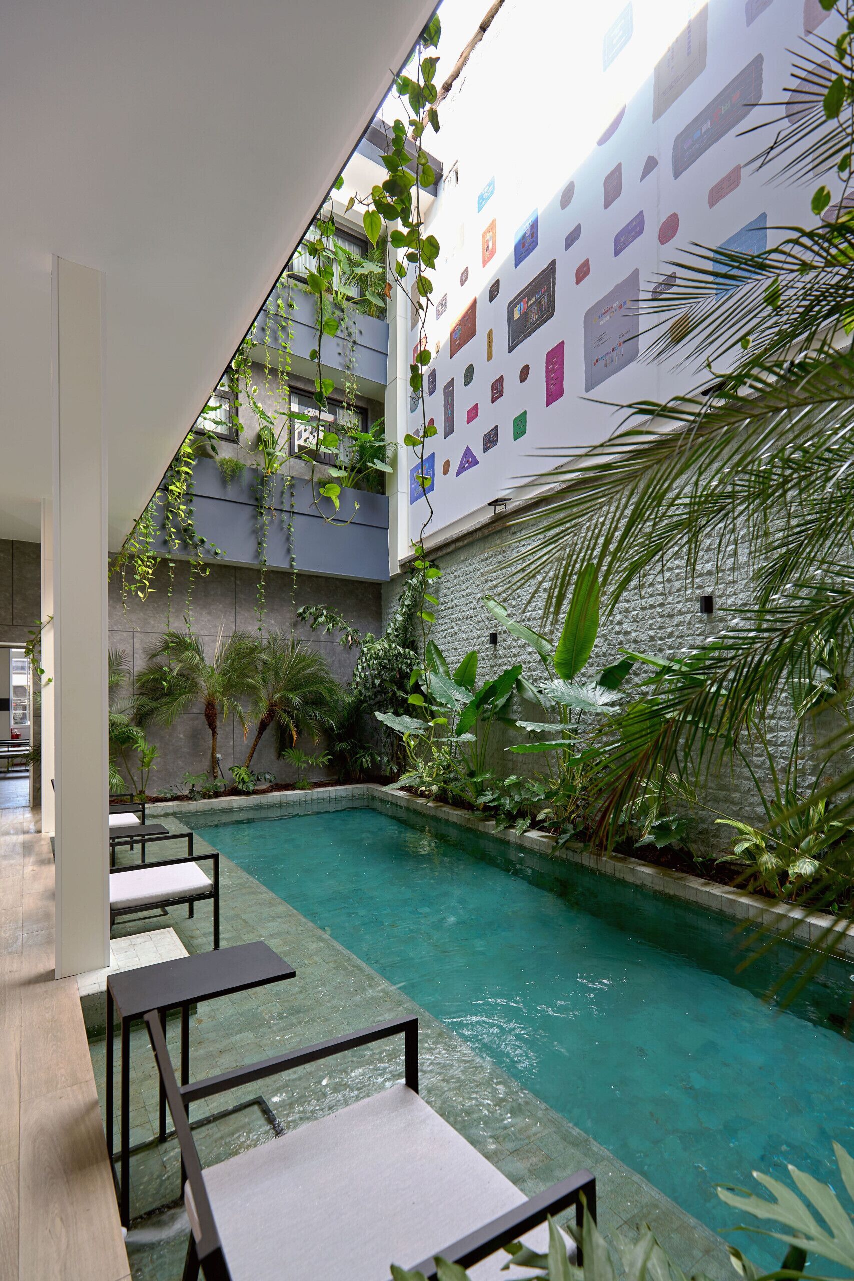 Un espace piscine intérieur moderne, agrémenté d’un mur au design géométrique, entouré d’une végétation luxuriante et de coins salon.