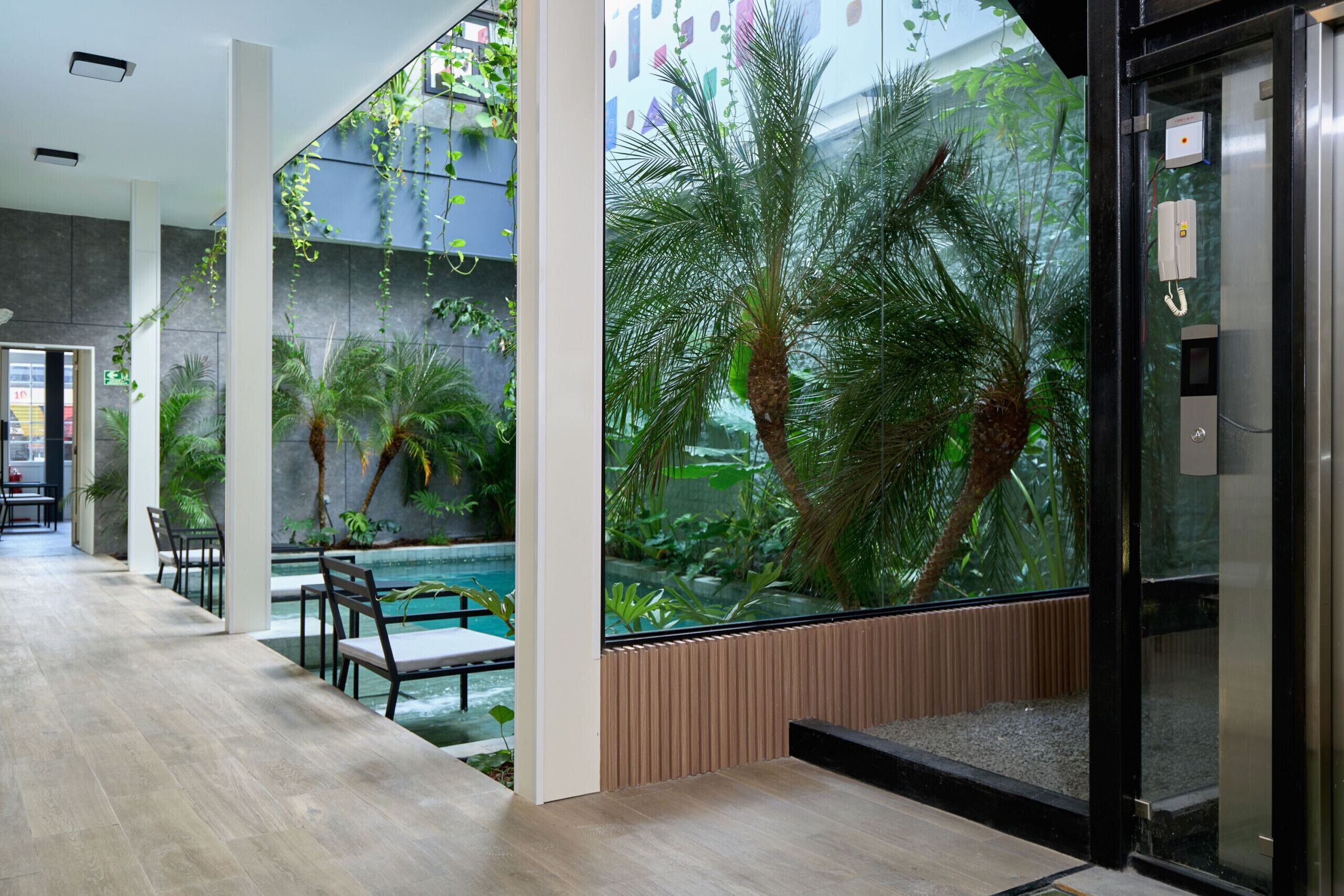 A modern indoor pool area with seating and a glass wall featuring tropical plants.