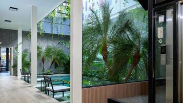 A modern indoor pool area with seating and a glass wall featuring tropical plants.