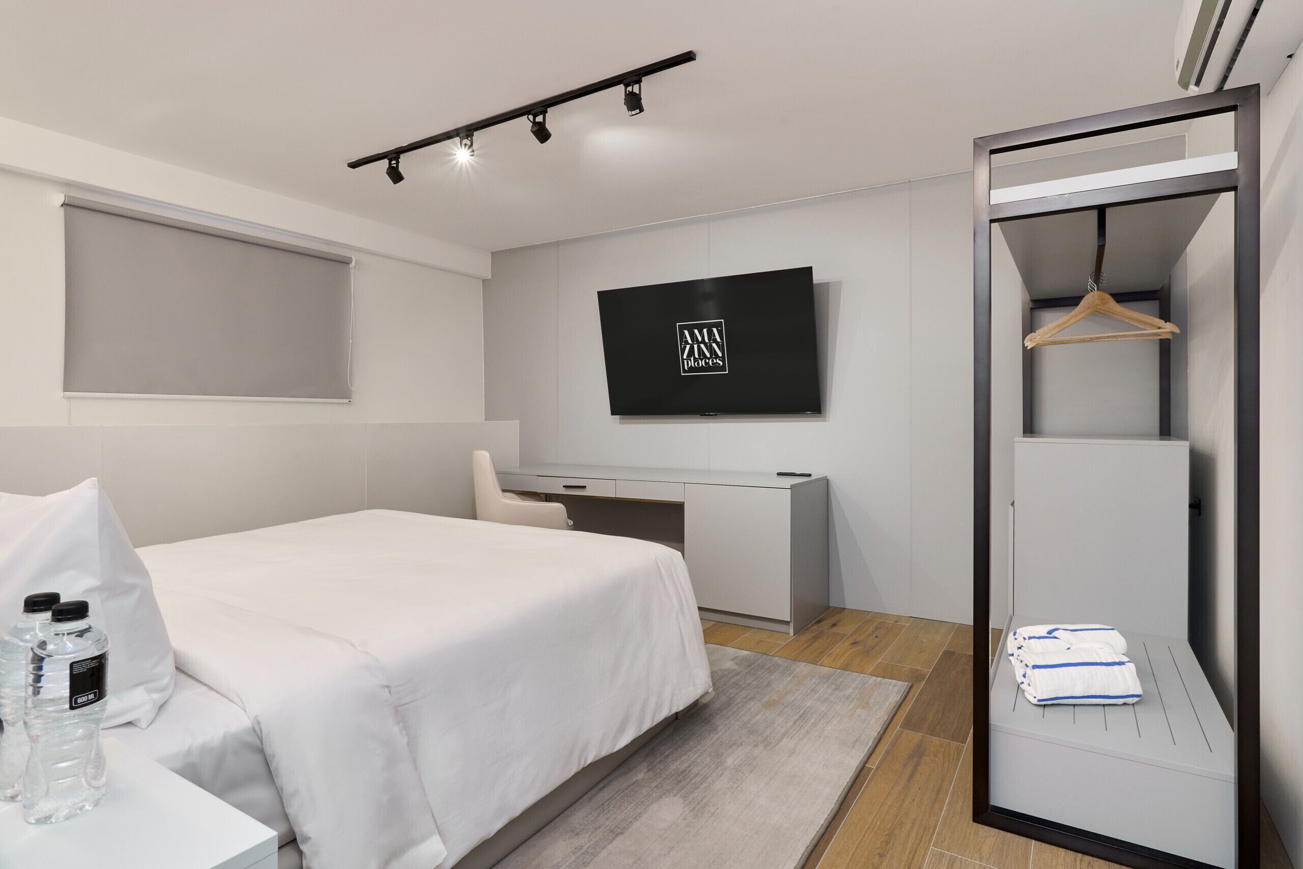 A modern hotel room with a bed, a desk, a TV, and a wardrobe.