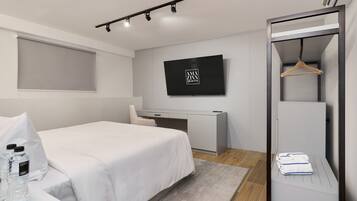 A modern hotel room with a bed, a desk, a TV, and a wardrobe.