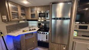 A compact kitchen with wooden cabinets, a stainless steel refrigerator, a microwave, and a gas stove. - Charming 2-bedroom campground in Key Largo with AC (Key Largo)