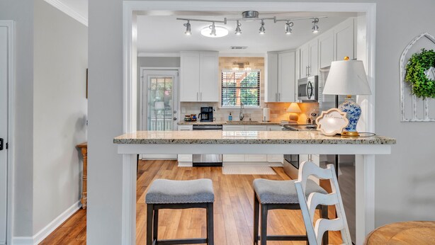 A modern kitchen with white cabinets, a granite countertop, and a central island with bar stools.