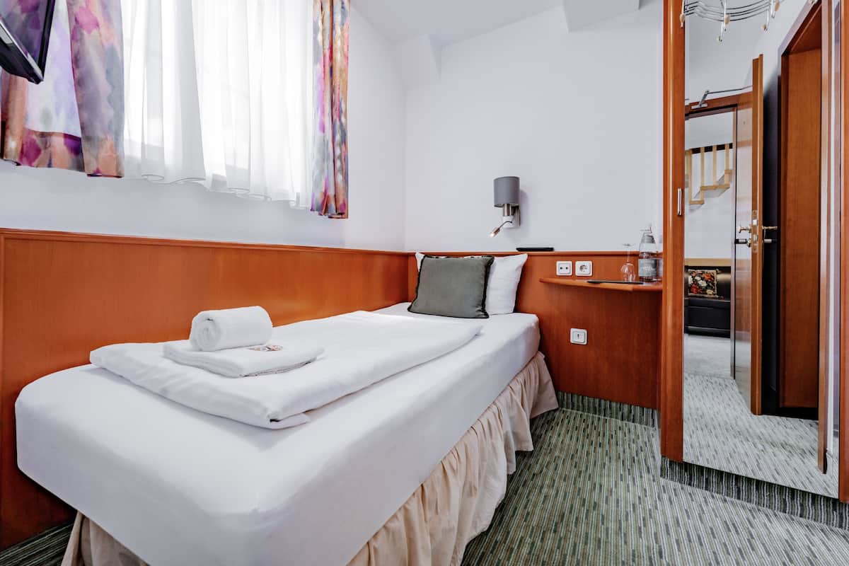 Una habitación de hotel con una cama bien hecha, una mesita de noche con una lámpara y un espejo.