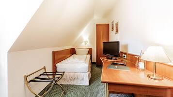 Una habitación de hotel pequeña y ordenada con una cama individual, un escritorio con computadora, una silla y una lámpara.