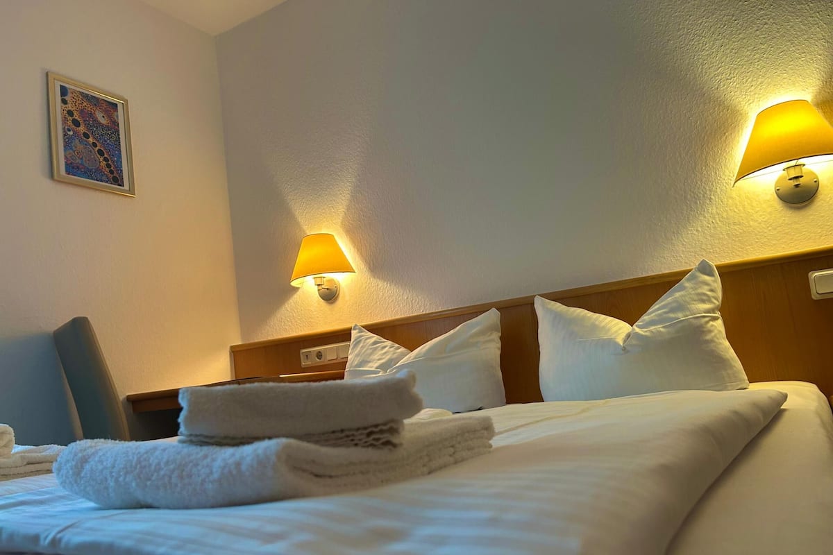 Una habitación de hotel con una cama bien hecha, dos lámparas de pared y un cuadro en la pared.
