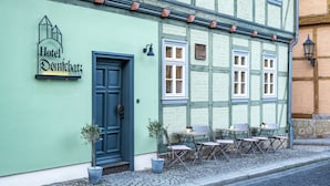 Ein Gebäude mit einem Schild, auf dem "Hotel Demichatz" steht, und einer blauen Tür. Draußen stehen Tische und Stühle bereit, sowie zwei Blumentöpfe.