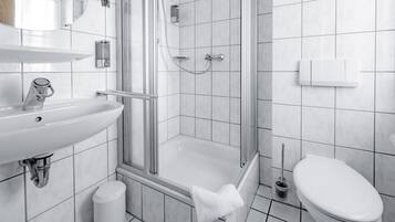 Un baño moderno con ducha de vidrio, un lavamanos blanco y un inodoro.
