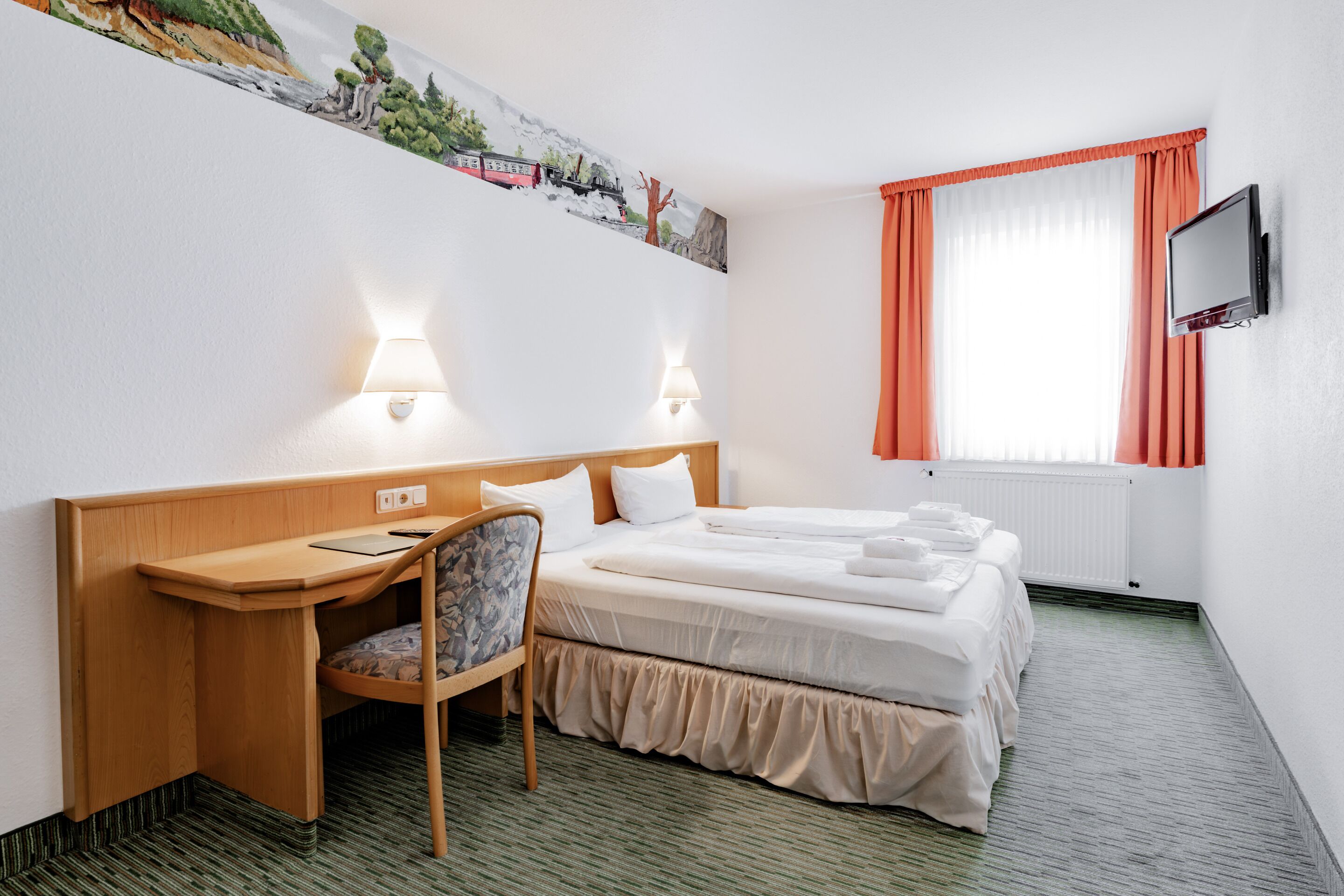 Une chambre d’hôtel avec un lit superposé, un bureau avec une chaise, un téléviseur à écran plat et un tableau au mur.