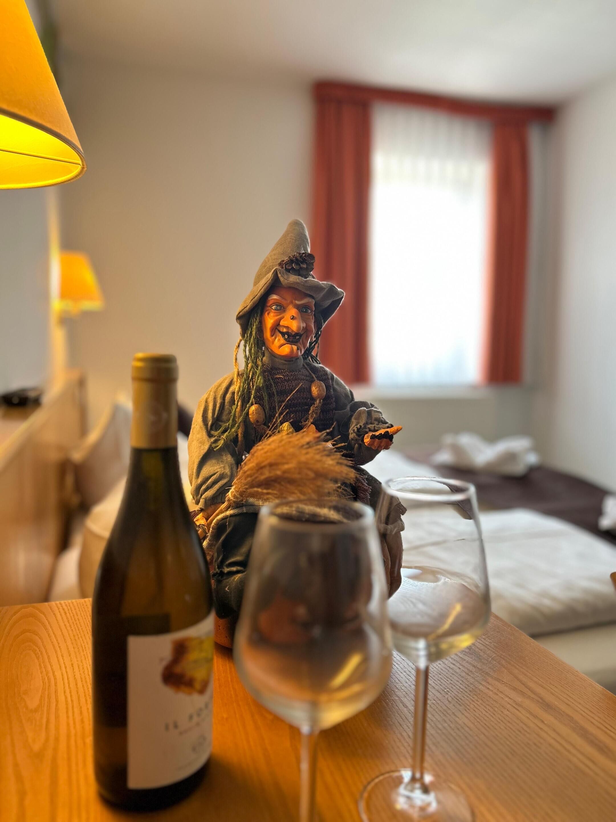 A room with a bed, a lamp, a wine bottle, and a wine glass on a wooden table.