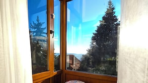 Una habitación con ventanas amplias, un taburete de madera redondo y vistas a árboles y edificios.