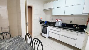 A compact kitchen with white cabinets, a black countertop, and a dining area with a marble table and chairs. - COOND0115 - Edifício Regina (Salvador)