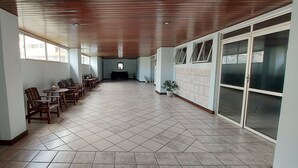 A spacious corridor with wooden ceiling, tiled floor, and rows of wooden chairs. - COOND0115 - Edifício Regina (Salvador)