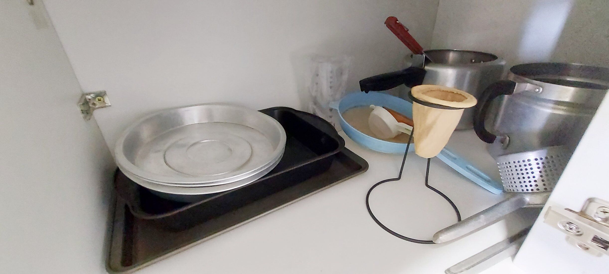 A kitchen with a stove, pots, pans, a strainer, and a tray.