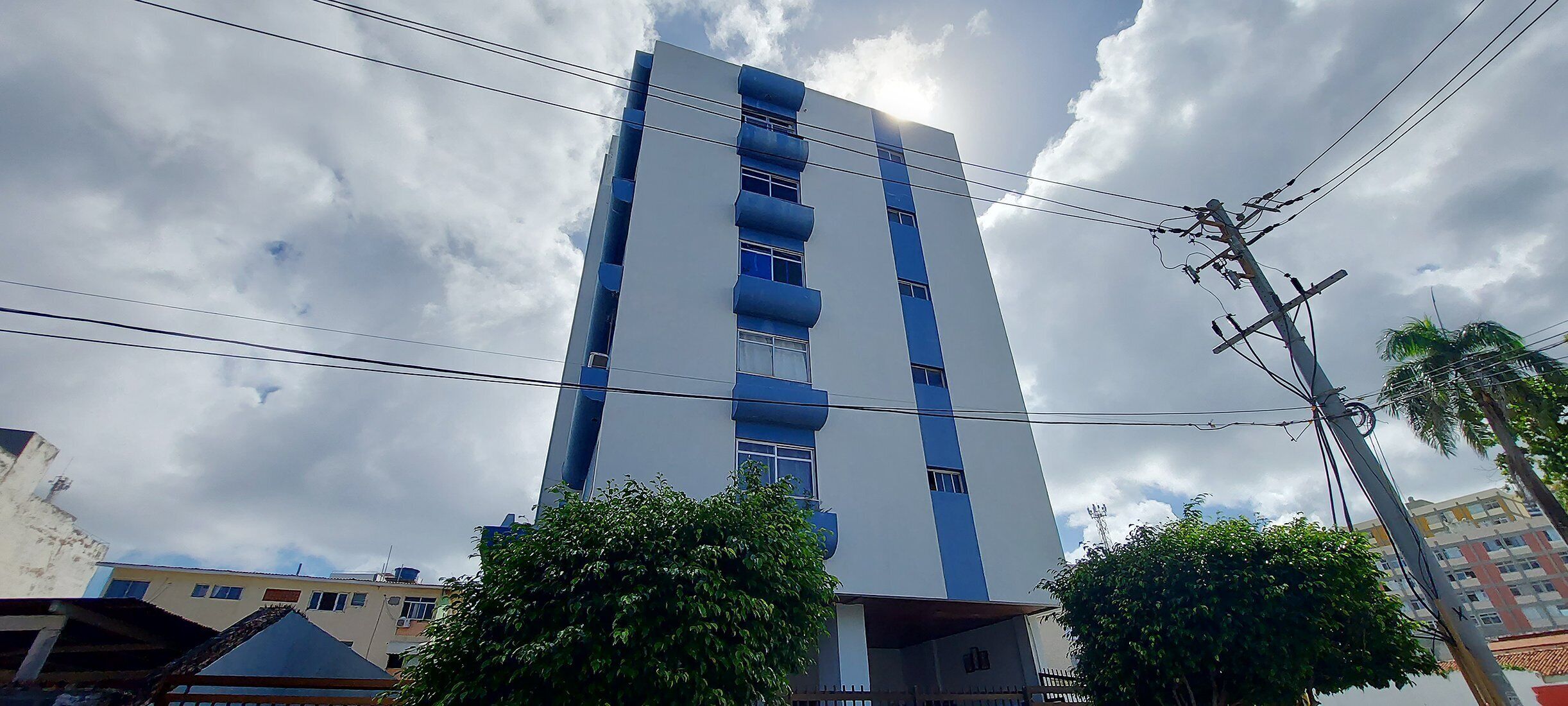 Um edifício alto com vários andares, rodeado por árvores e outros edifícios.