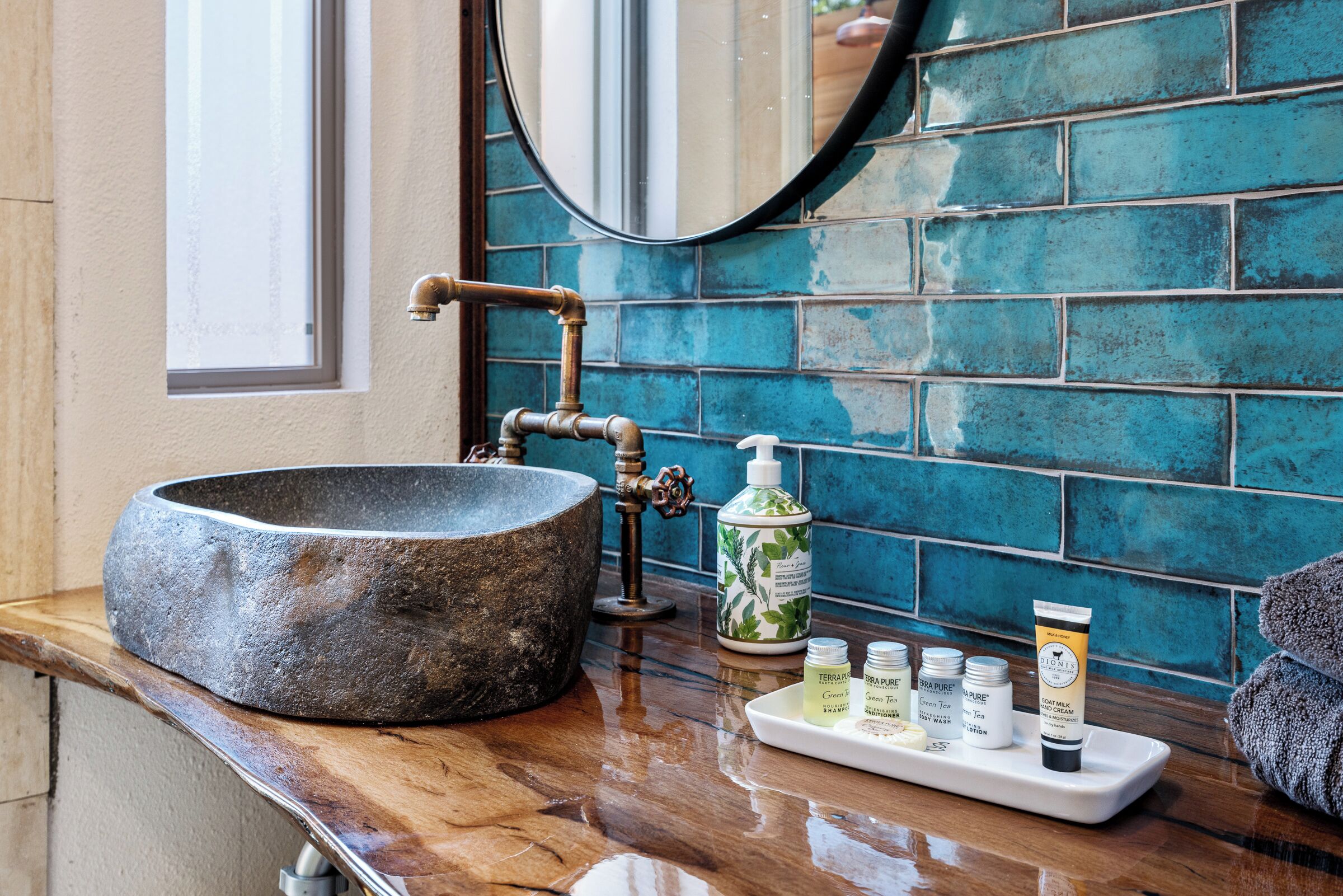 A bathroom with a stone sink, a mirror, and a shelf with toiletries.