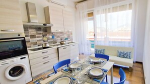 Une cuisine moderne équipée d’un lave-linge, un coin repas avec une table pour quatre personnes et un canapé agrémenté de coussins à motifs.