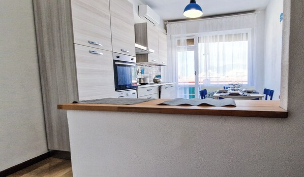 A modern kitchen with white cabinets, a wooden countertop, and a dining area with blue chairs. - Sea view 2 steps away from everything. 21A (Lavagna)