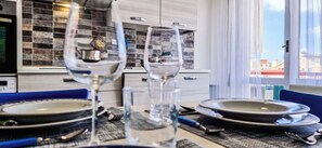 A dining table set with plates, glasses, and cutlery, with a view of a cityscape through a window. - Sea view 2 steps away from everything. 21A (Lavagna)