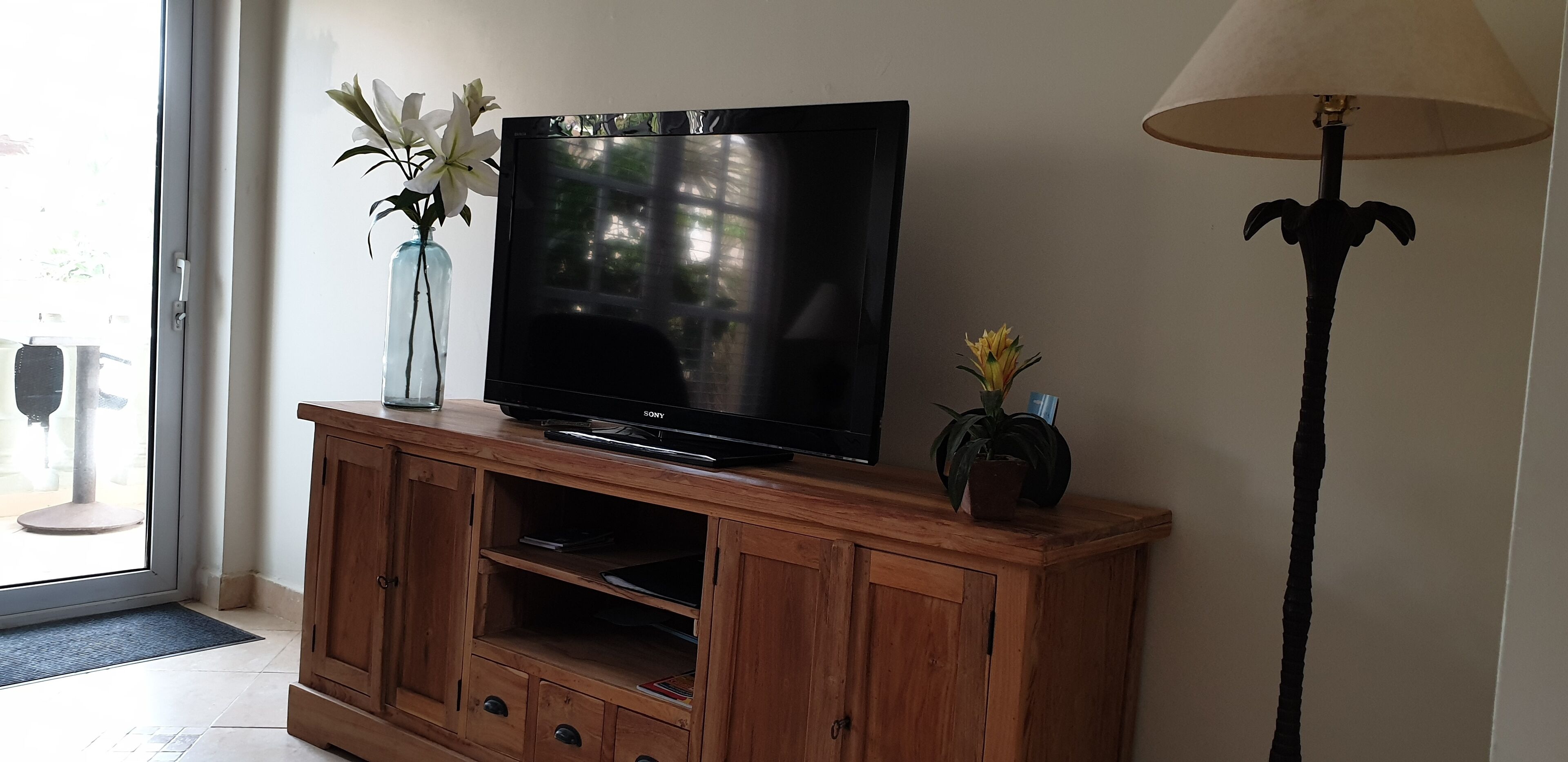 Un televisor sobre un mueble de madera, con un florero y una lámpara a un lado.