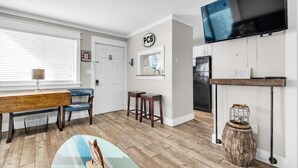 A modern kitchen with a flat-screen TV, wooden flooring, a bench, and bar stools. - Sand Castles West II G4- Finview (Panama City Beach)