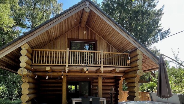 A log cabin with a balcony, outdoor seating area, and a hot tub. - The Loghouse between Ghent and Bruges (Aalter)