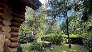 A log cabin with a stone foundation, surrounded by a lush garden with various shrubs and trees. - The Loghouse between Ghent and Bruges (Aalter)