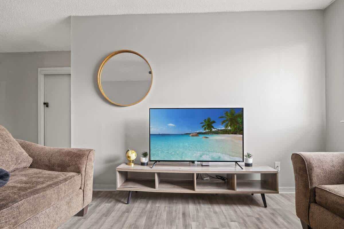 A living room with a flat-screen TV on a wooden stand, a round mirror on the wall, and two sofas.