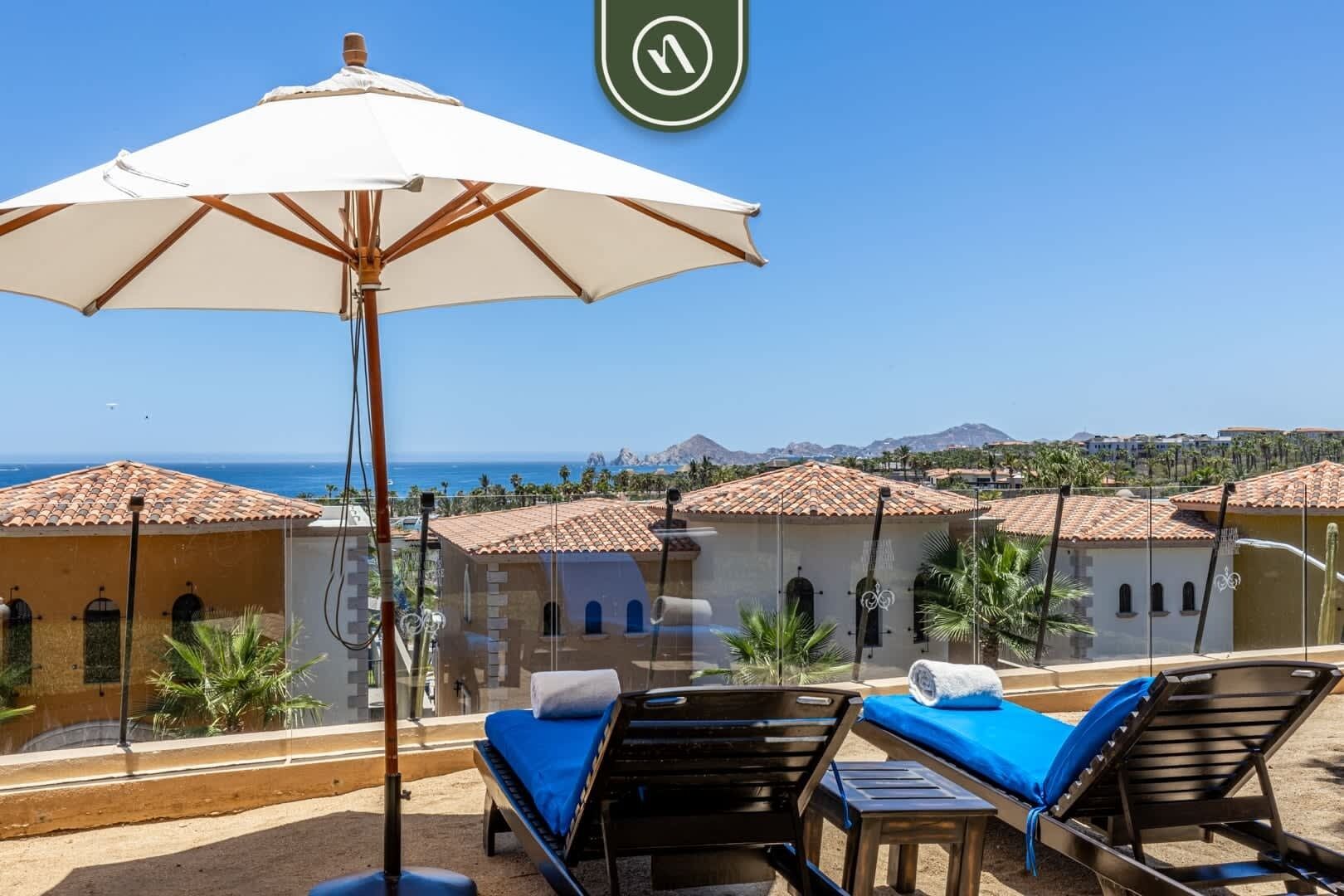 A balcony with a white umbrella, lounge chairs, and a view of the sea and buildings.