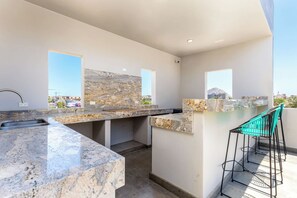 A modern kitchen with a marble countertop, a sink, and a bar area with a chair.
