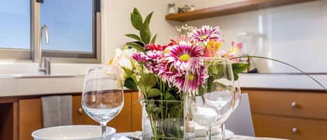 A dining table set with white plates, two wine glasses, and a vase with pink and white flowers.