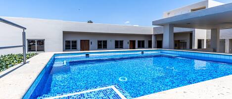 Una piscina rettangolare con piastrelle blu, circondata da un edificio bianco con numerose finestre e porte.