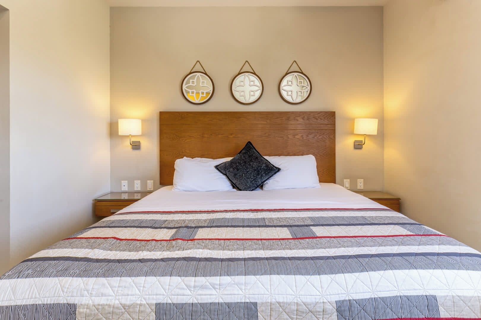 Ein Hotelzimmer mit einem Holzkopfteil, einer gesteppten Bettdecke und drei Wandleuchten.